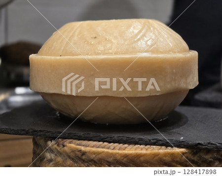 Rustic artisan cheese wheel for culinary and cheese tasting enthusiasts. World Cheese Day. Close-up Rustic artisan cheese wheel for culinary and cheese tasting enthusiasts. World Cheese Day. Close-up 128417898