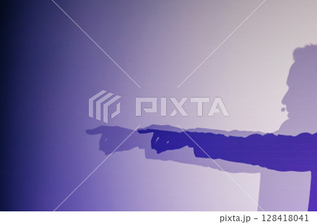 Silhouette of person pointing with dramatic shadows on purple gradient background 128418041