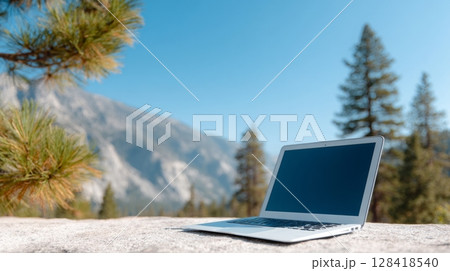 Laptop placed on a rock surface in a serene outdoor setting, surrounded by tall trees and mountains, ideal for a workcation experience Laptop placed on a rock surface in a serene outdoor setting, surrounded by tall trees and mountains, ideal for a workcation experience 128418540