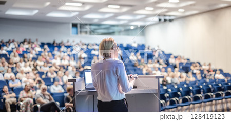 Female speaker giving a talk on corporate business conference. Unrecognizable people in audience at conference hall. Business and Entrepreneurship event 128419123