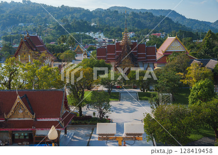 Wat Chalong in Phuket, Thailand, features ornate red and gold roofs, a central pagoda, lush greenery, and forested hills in the background. 128419458