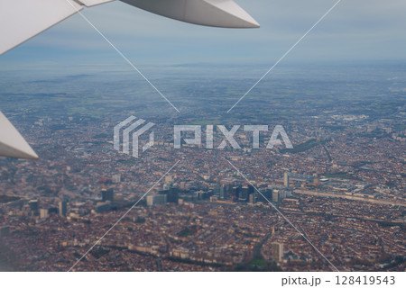 Aerial perspective of Brussels featuring skyscrapers, low rise buildings, a central park, and surrounding countryside, with a plane wing visible. Aerial perspective of Brussels featuring skyscrapers, low rise buildings, a central park, and surrounding countryside, with a plane wing visible. 128419543
