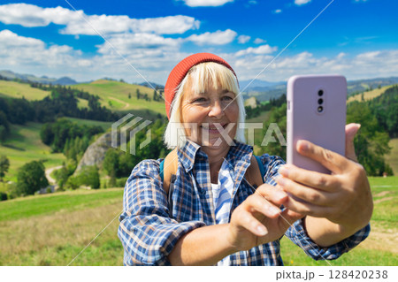 Smiling senior woman taking a selfie during a hiking adventure in the mountains 128420238