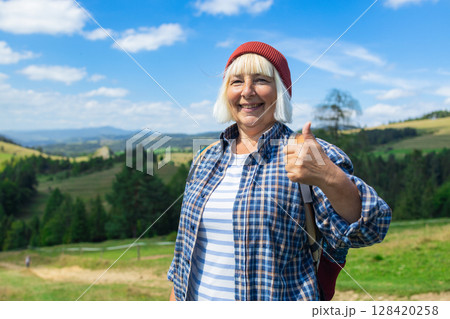 Smiling senior woman giving thumbs up while hiking in the mountains 128420258