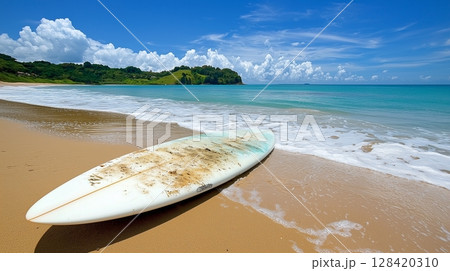 A surfboard lying on the beach, with a blue sky and calm sea on the background. A surfboard lying on the beach, with a blue sky and calm sea on the background. 128420310