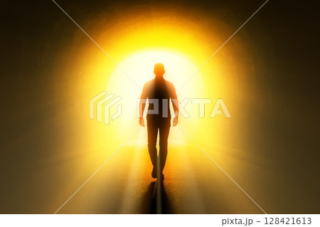 Silhouette of person walking through dark tunnel towards bright yellow light, a concept for hope, new life, and future success 128421613