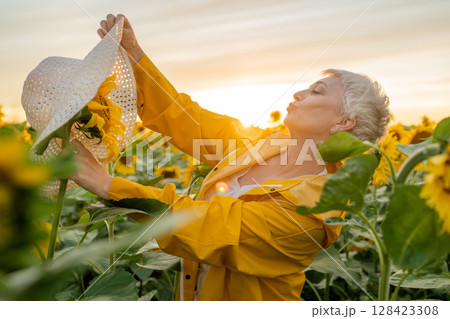 A Joyful Woman playfully puts hat on sunflower in a Field of Sunflowers is Celebrating the Natural Beauty Around Her 128423308