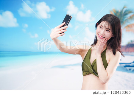 快晴のビーチでスマホで自撮りをする水着を着た若い女性 快晴のビーチでスマホで自撮りをする水着を着た若い女性 128423360