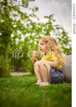 Girl sitting quietly with ice cream on green grass 128423433