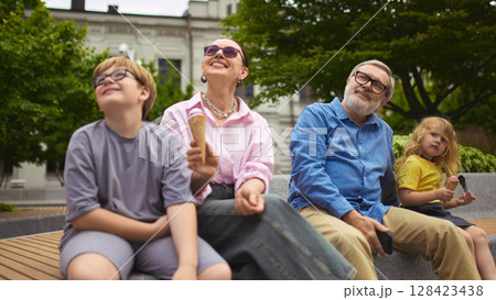 Grandparents and grandchildren sitting on bench with ice cream outdoors Grandparents and grandchildren sitting on bench with ice cream outdoors 128423438