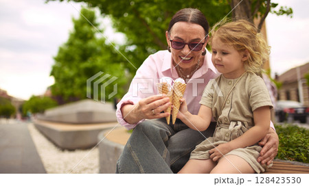 Melting memories. Grandmother and little girl comparing ice cream cones joyfully Melting memories. Grandmother and little girl comparing ice cream cones joyfully 128423530
