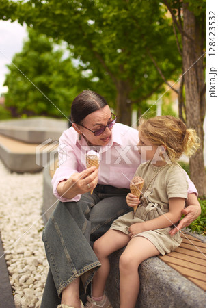 Hug and scoop. Grandma and granddaughter share ice cream outdoors 128423532