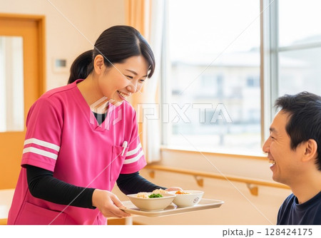 障がい者施設で食事を配膳する笑顔の女性介護士 配膳、ランチタイム、給食、食事、楽しみ 128424175