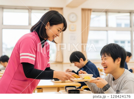 障がい者施設で食事を配膳する笑顔の女性介護士 配膳、ランチタイム、給食、食事、楽しみ 128424176