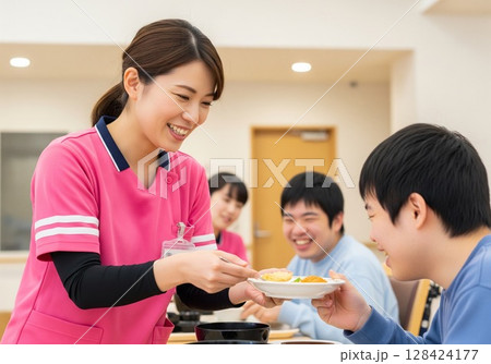 障がい者施設で食事を配膳する笑顔の女性介護士 配膳、ランチタイム、給食、食事、楽しみ 128424177