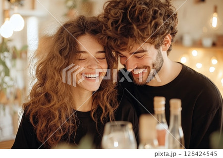 Joyful Couple Laughing Together in Cozy Kitchen Setting   Young happy modern couple enjoying time and while cooking or preparing a meal in a warm domestic home environment 128424545