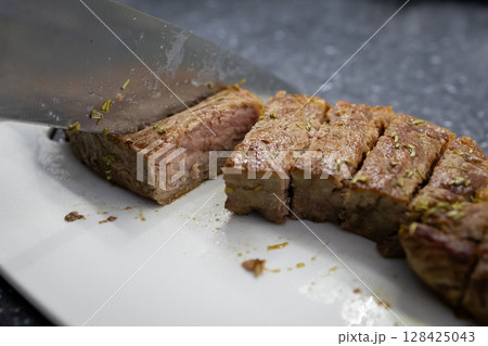 A sharp kitchen knife expertly slicing a juicy cooked beef tenderloin roast on a white cutting board, highlighting delicious culinary preparation for a healthy meal A sharp kitchen knife expertly slicing a juicy cooked beef tenderloin roast on a white cutting board, highlighting delicious culinary preparation for a healthy meal 128425043