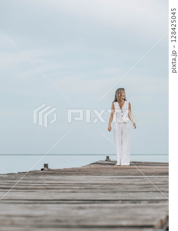 Asian woman in white outfit stands on wooden pier, calm lake, peaceful overcast, viewed from behind with contemplative mood, mindfulness, travel retreats, wellness, vertical, copy space Asian woman in white outfit stands on wooden pier, calm lake, peaceful overcast, viewed from behind with contemplative mood, mindfulness, travel retreats, wellness, vertical, copy space 128425045