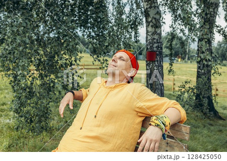 man in yellow hoodie and red cap resting with closed eyes on wooden bench under birch trees during warm summer day in rural outdoor area concept of vacation travel wellness retreat man in yellow hoodie and red cap resting with closed eyes on wooden bench under birch trees during warm summer day in rural outdoor area concept of vacation travel wellness retreat 128425050