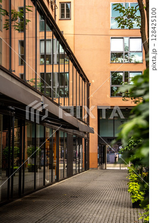 Modern Street Scene In Munich Center: Contemporary Architecture With Glass Facades And Greenery In A Quiet Urban Courtyard Modern Street Scene In Munich Center: Contemporary Architecture With Glass Facades And Greenery In A Quiet Urban Courtyard 128425100