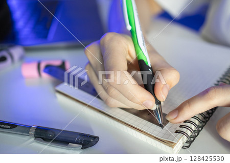 Student's hand diligently using a green pen and ruler on a grid notebook, illustrating academic precision, focused learning, and effective study methods 128425530