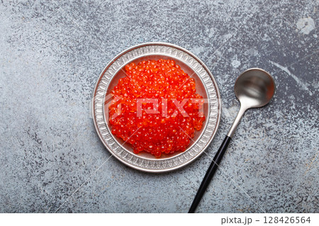 Small metal plate with red salmon caviar and a spoon top view on grey concrete background, festive luxury delicacy and appetizer 128426564
