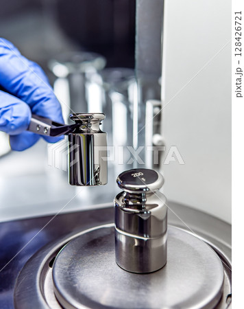 A operator's hand is holding steel calibration weight to place on the analytical balance. A operator's hand is holding steel calibration weight to place on the analytical balance. 128426721