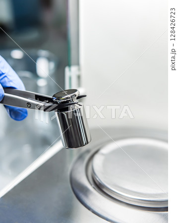 A operator's hand is holding steel calibration weight to place on the analytical balance. Concept of quality control in a laboratory. 128426723