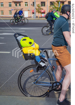 Man riding bicycle with small child in bright helmet and safety seat on city street during family cycling day. Concept of cycling, safety, cycling, active urban parenting with kids Man riding bicycle with small child in bright helmet and safety seat on city street during family cycling day. Concept of cycling, safety, cycling, active urban parenting with kids 128426776