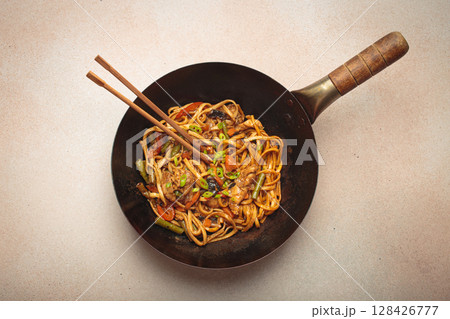 Asian style stir fry noodles with chicken and vegetables in a black wok pan with chopsticks 128426777