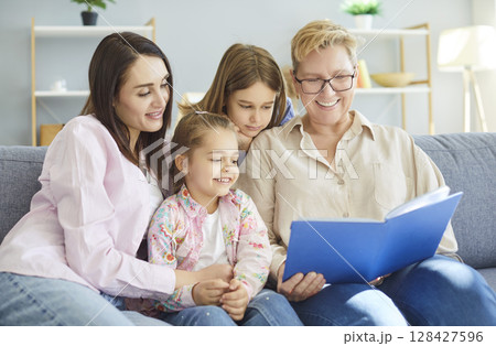 Family sitting on sofa at home looking through a photo album enjoying good memories Family sitting on sofa at home looking through a photo album enjoying good memories 128427596