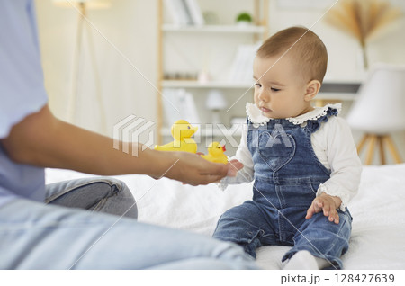 Newborn baby and mother play with yellow ducks, child sitting looking with curiosity at new toys Newborn baby and mother play with yellow ducks, child sitting looking with curiosity at new toys 128427639