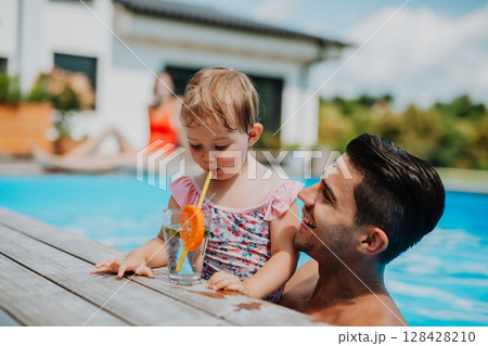 Father and young daughter drinking water while playing in pool. 128428210