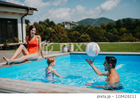 Young family with small daughter in swimming pool outdoors in backyard garden. 128428211