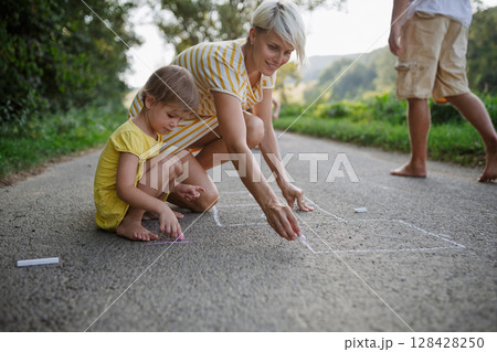 Mom and girl drawing with chalk on road. . 128428250