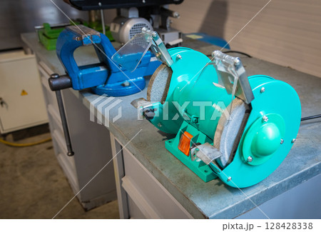 Bench grinder sitting on workbench next to vise in workshop 128428338