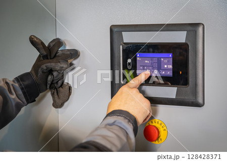 Technician operating industrial control panel with touchscreen and emergency button Technician operating industrial control panel with touchscreen and emergency button 128428371