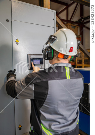 Technician operating industrial control panel wearing safety equipment 128428372