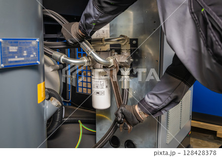 Technician repairing industrial compressor using a wrench 128428378