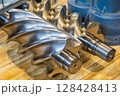 Shiny new screw compressor rotor resting on wooden table 128428413