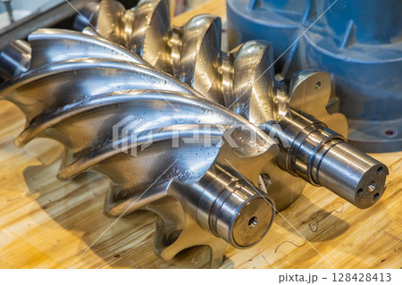 Shiny new screw compressor rotor resting on wooden table Shiny new screw compressor rotor resting on wooden table 128428413
