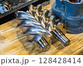 Shiny new screw compressor rotor resting on wooden workbench 128428414