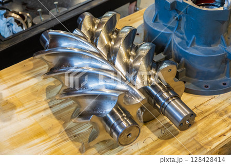 Shiny new screw compressor rotor resting on wooden workbench Shiny new screw compressor rotor resting on wooden workbench 128428414