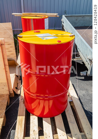 Red and yellow metal barrels resting on wooden pallet 128428419