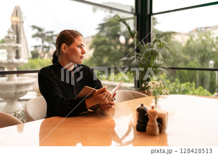 Woman Restaurant Menu: Woman reads menu in restaurant, daydreaming near the fountain, during daylight hours. 128428513