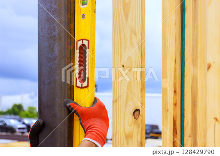 Worker checks vertical alignment of wooden beams using spirit level at construction site during work time 128429790
