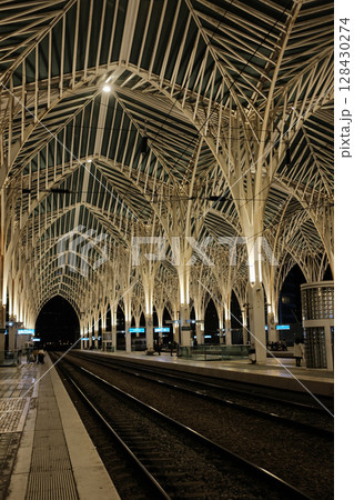 Modern illuminated architecture of Oriente Station at night in Lisbon Portugal featuring geometric roof design arches and empty railway tracks in futuristic urban environment. High quality photo 128430274