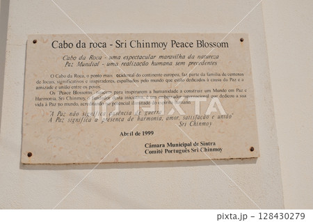 Commemorative stone plaque at Cabo da Roca westernmost point of continental Europe in Sintra Portugal historical marker with text tribute by Sri Chinmoy peace blossom. High quality photo 128430279