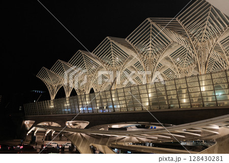 Modern illuminated architecture of Oriente Station at night in Lisbon Portugal featuring geometric roof design arches and empty railway tracks in futuristic urban environment. High quality photo 128430281