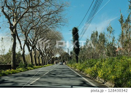 Scenic coastal road with view of Cabo da Roca lighthouse in Sintra Portugal curving highway through natural cliffs overlooking Atlantic Ocean under clear blue sky 128430342
